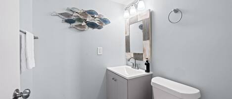 A bathroom with a toilet, sink, and mirror. There is a towel rack and a wall-mounted light fixture.