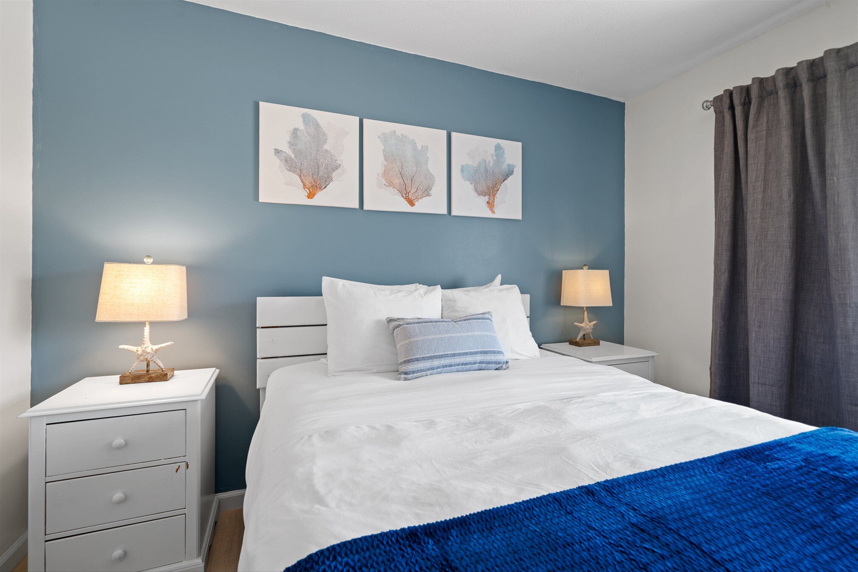 Une chambre à coucher comprenant un lit, deux tables de chevet, une commode et un mur orné de trois œuvres d’art.