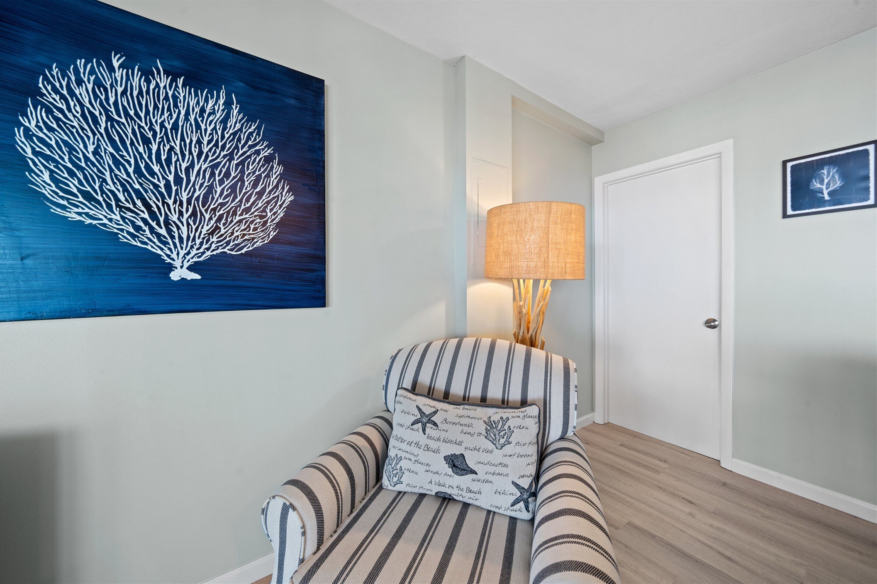 A room with a striped armchair, a wall-mounted lamp, a framed picture, and a large artwork of a coral reef.