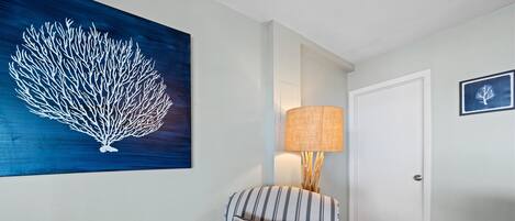A room with a striped armchair, a wall-mounted lamp, a framed picture, and a large artwork of a coral reef.