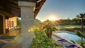 Un área junto a la piscina con vista al atardecer, un pilar de concreto y un patio con sillas.