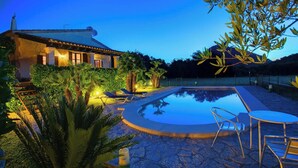 Una villa con piscina, rodeada de abundante vegetación y con montañas al fondo.