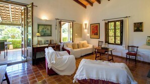 Una habitación acogedora con techo de madera, un sofá, una mesa y una silla. Hay ventanas con cortinas, un cuadro en la pared y una puerta que da a un espacio exterior.