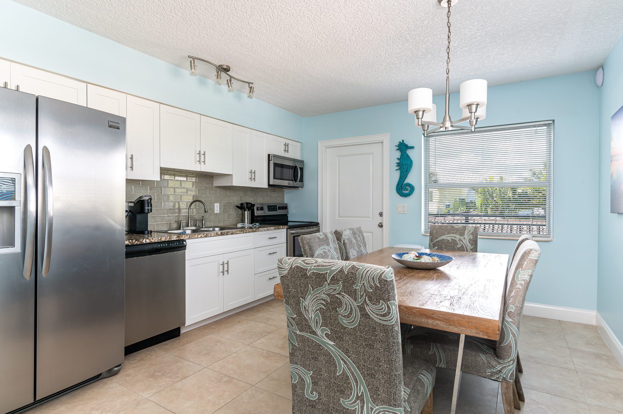 A modern kitchen with white cabinets, stainless steel appliances, and a dining area with patterned chairs and a wooden table.
