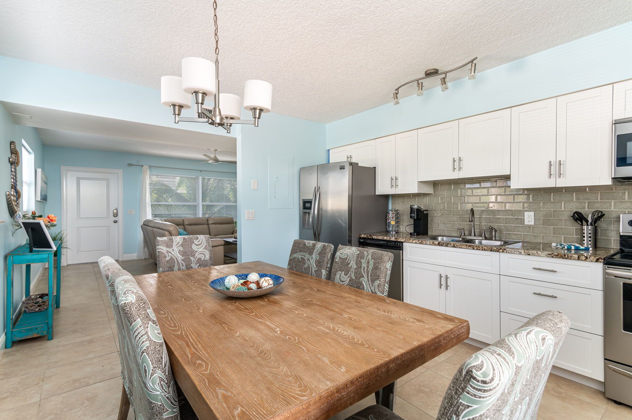 A modern kitchen with white cabinets, a stainless steel refrigerator, and a wooden dining table with patterned chairs.