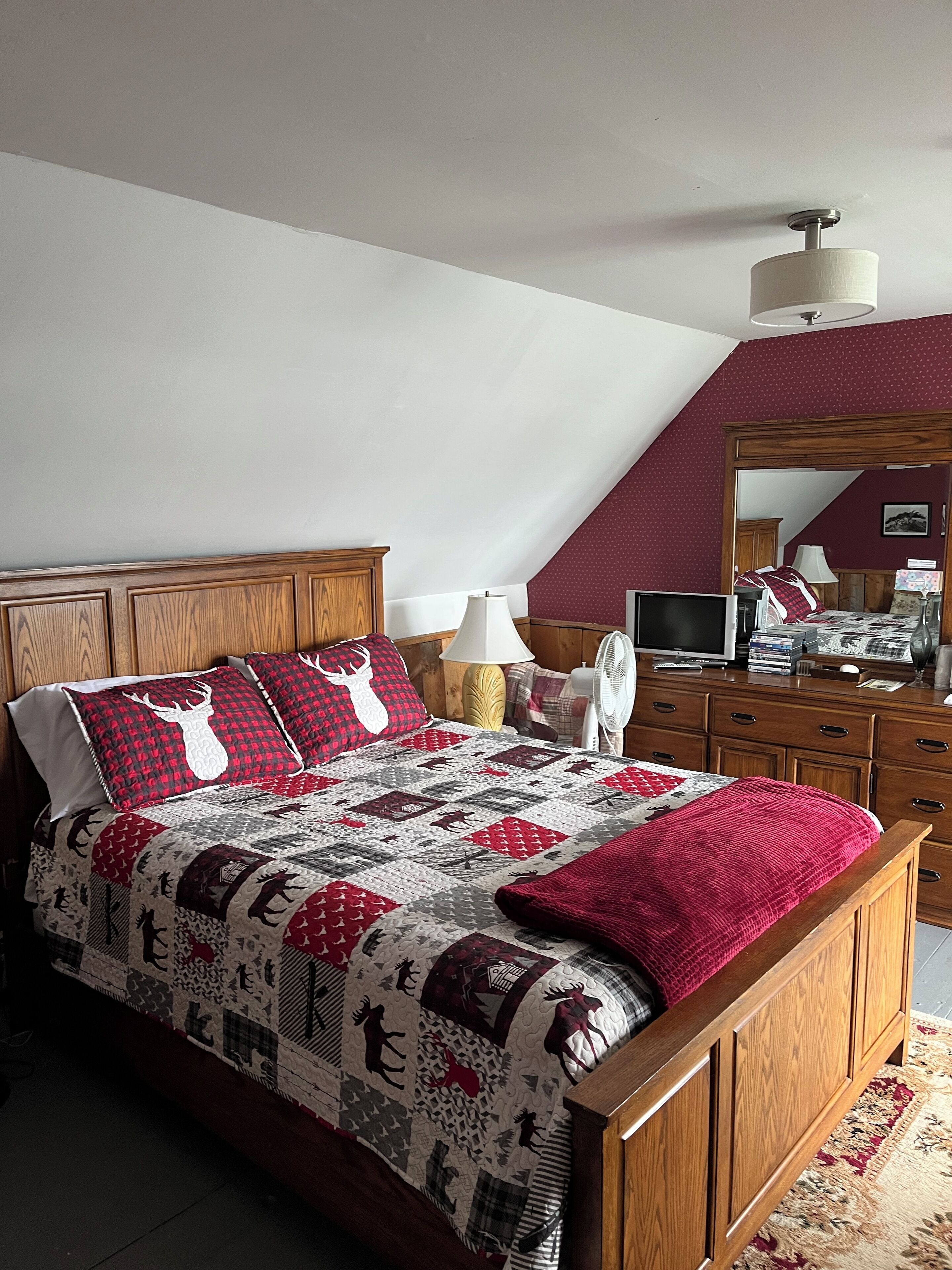 Una camera da letto con un letto di legno, una coperta rossa e bianca, uno specchio, una scrivania e una sedia.