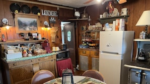 A cozy lodge kitchen with wooden cabinets, a refrigerator, a stove, and a dining table set with placemats. - Seymour Lake Lodge (Morgan)