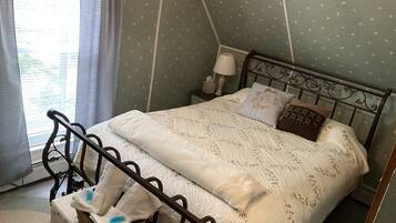 A neatly made bed with a white quilt and decorative pillows, a bedside table with a lamp, and a window with curtains.