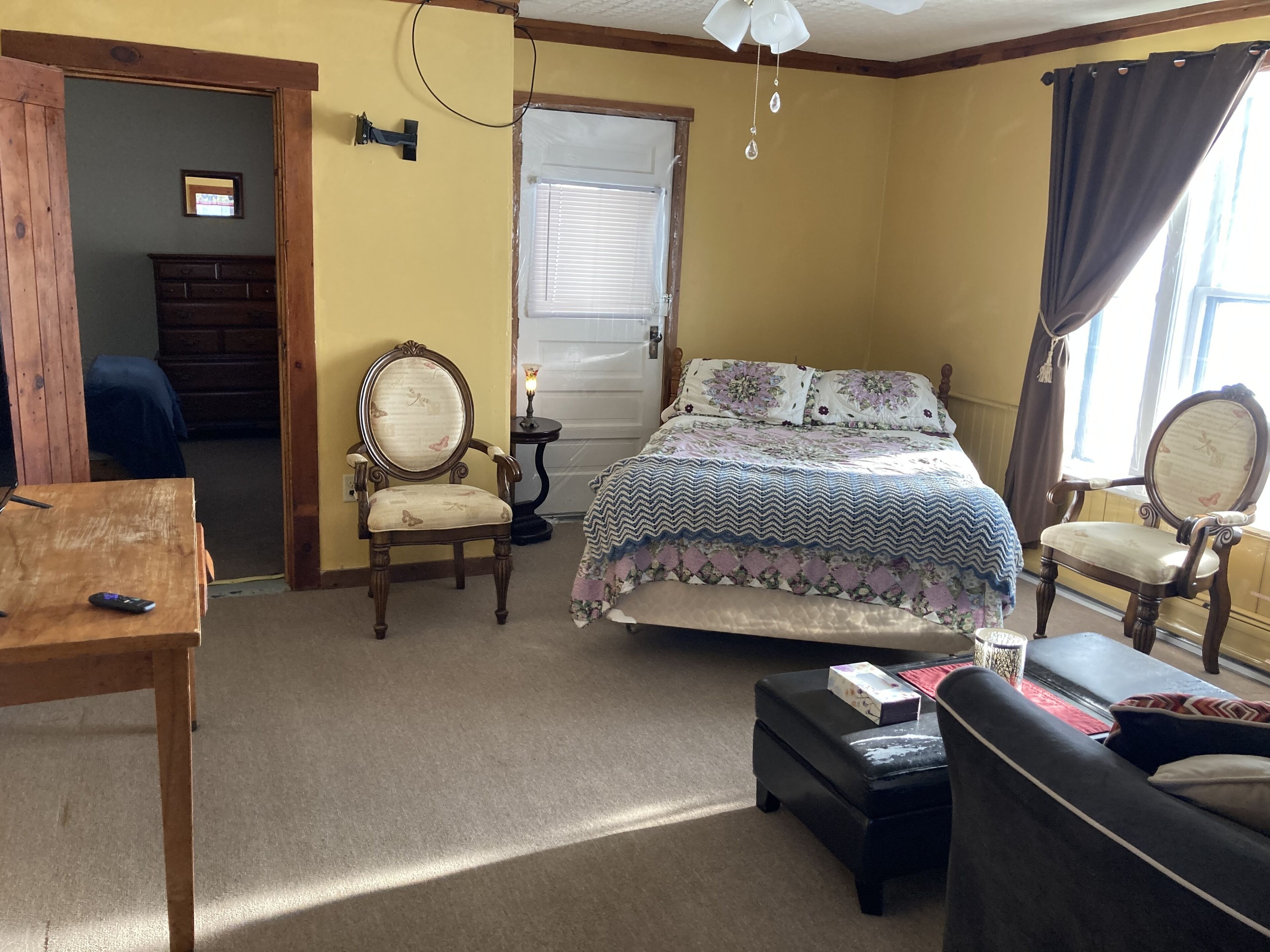 A bedroom with a bed, two chairs, a table, and a dresser.