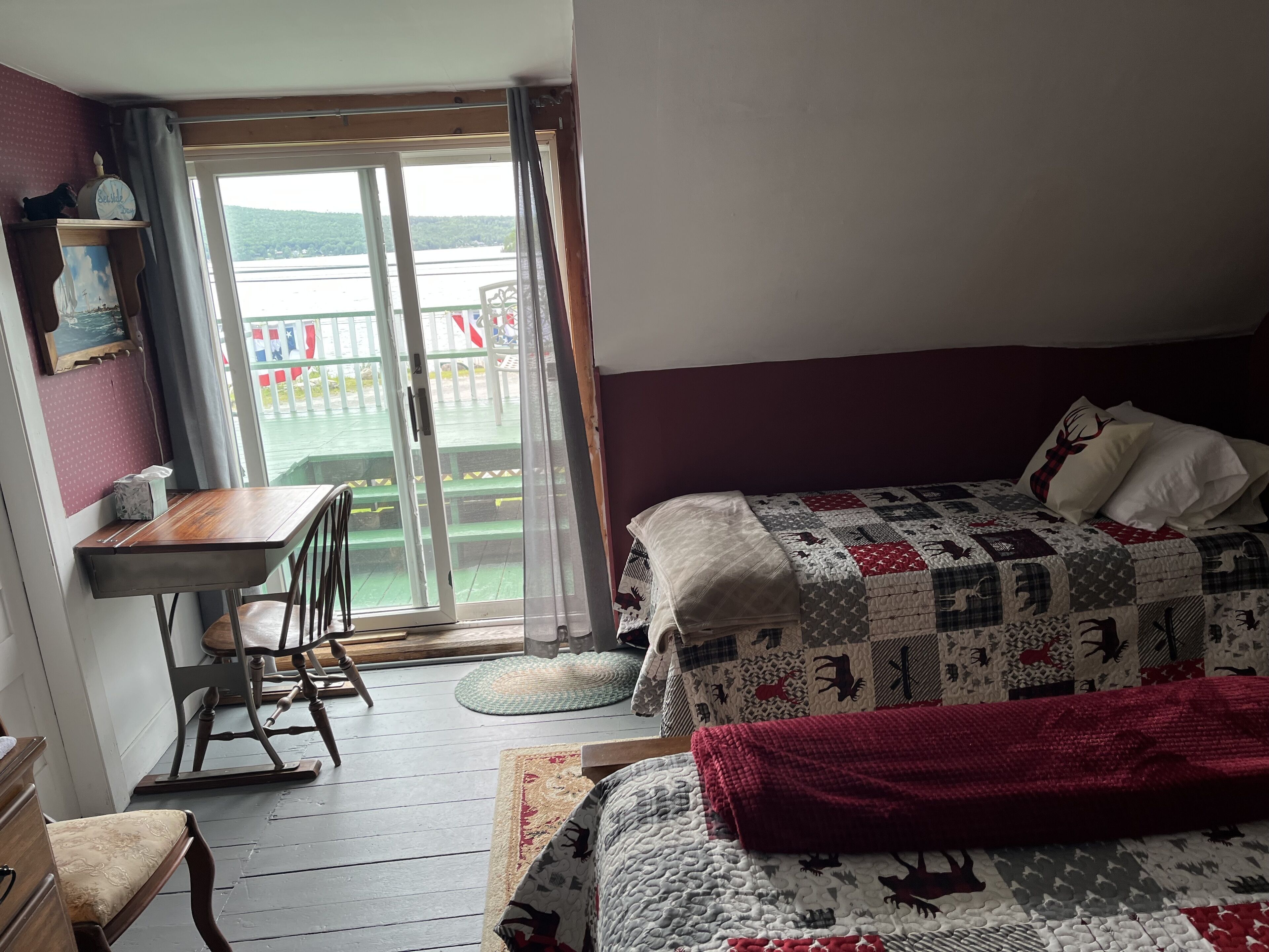 A bedroom with a bed, a desk, and a chair. There is a view of a balcony with a railing and a table outside.