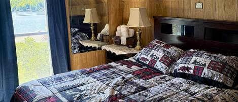 Un dormitorio con cama, ventilador de techo, ventana con cortinas y vistas al exterior.