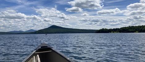 A boat on a calm lake with a mountain and forest in the background.