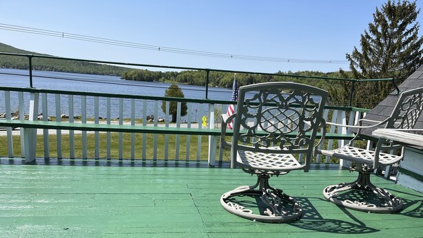 A green deck with two ornate chairs and a table, overlooking a lake with a white fence and trees in the background. - Seymour Lake Lodge (Morgan)