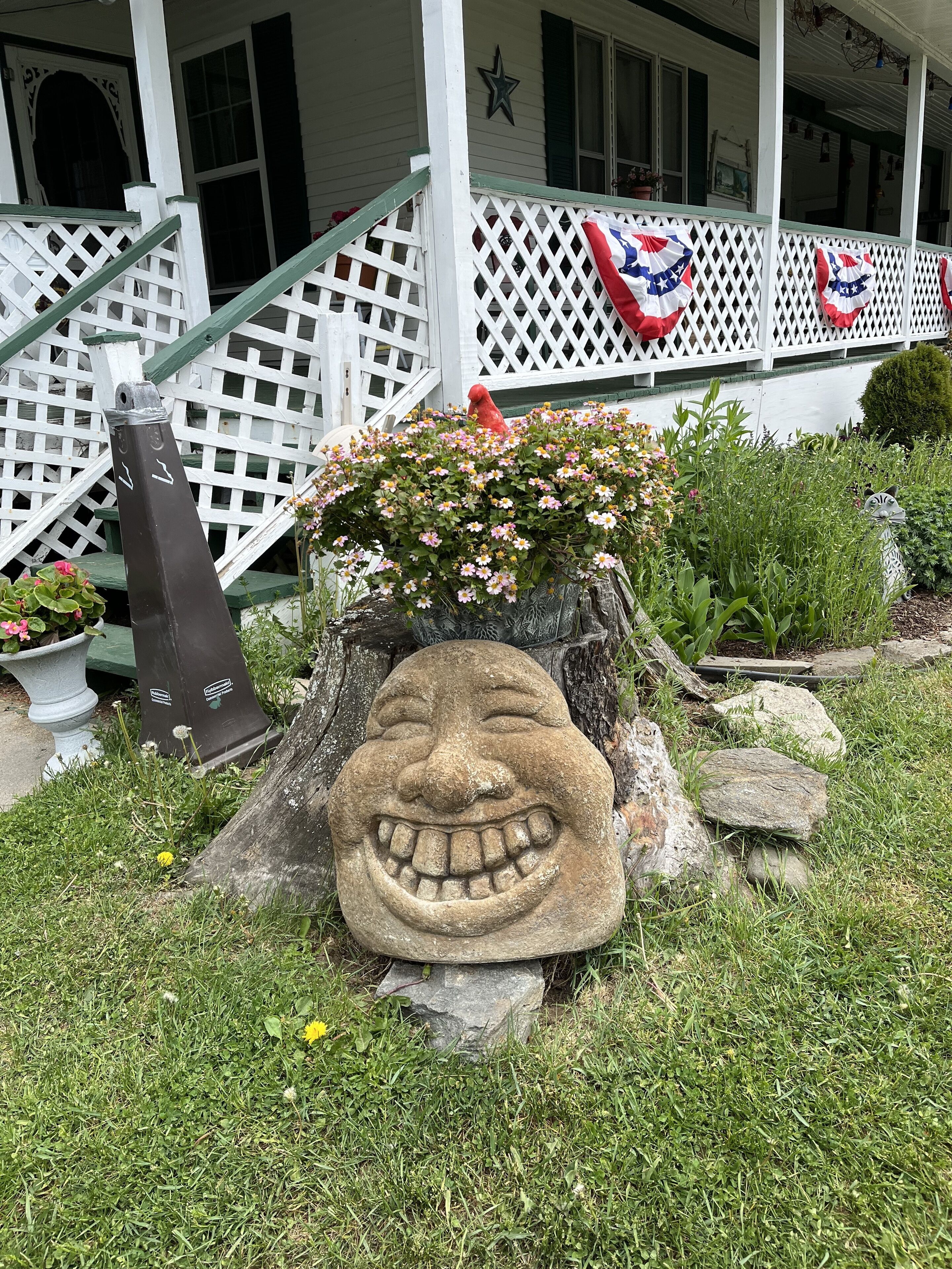 En veranda med en stenhovedskulptur, et hvidt hegn og en rød fuglestatue.