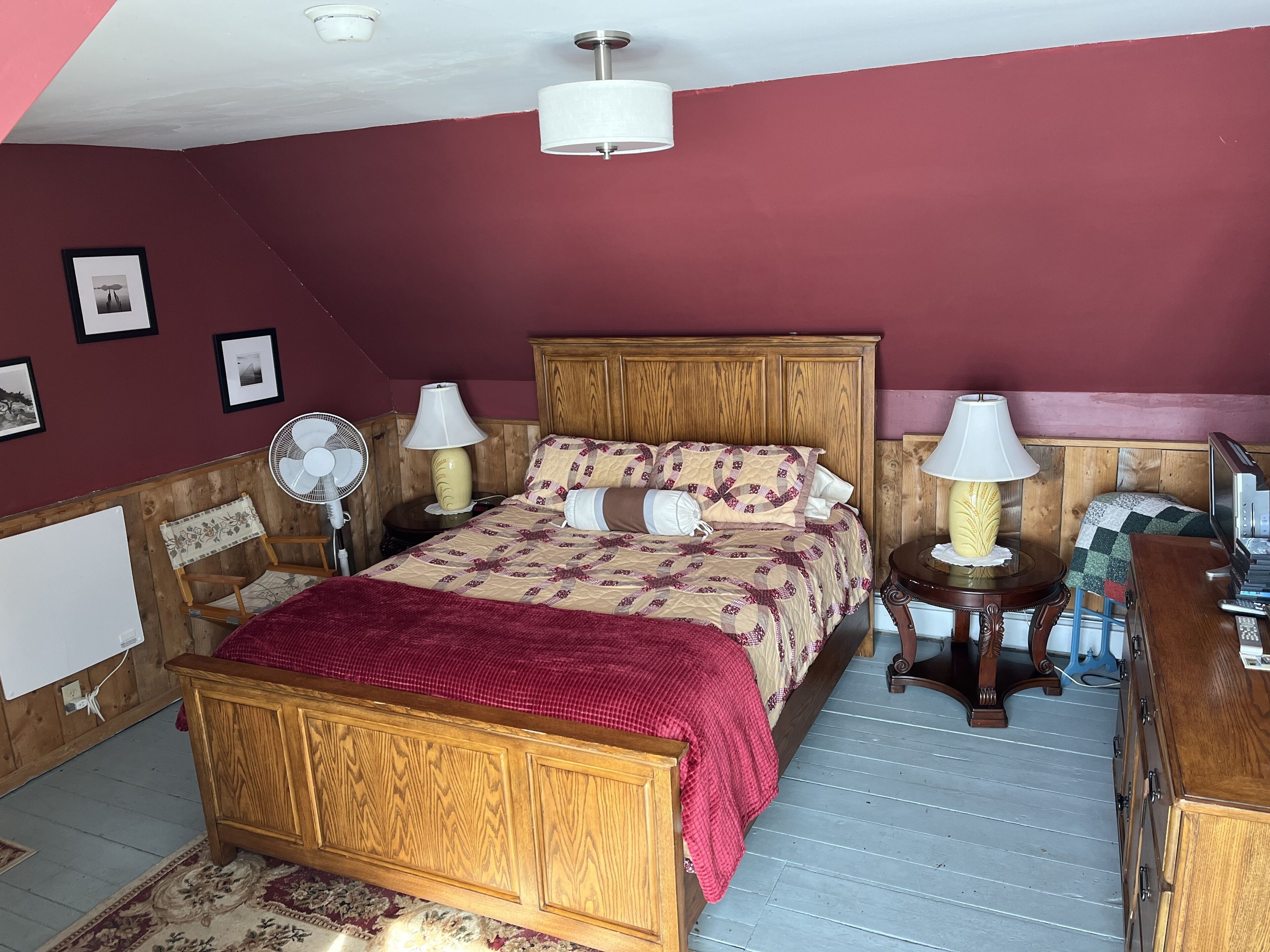 A bedroom with a wooden bed, two bedside tables with lamps, a ceiling fan, and a television on a wooden dresser.