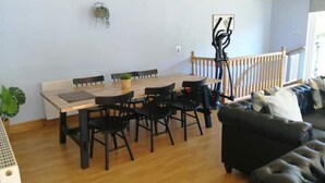 Un coin repas avec une table en bois et des chaises noires, un canapé noir et un escalier doté d’une rampe.
