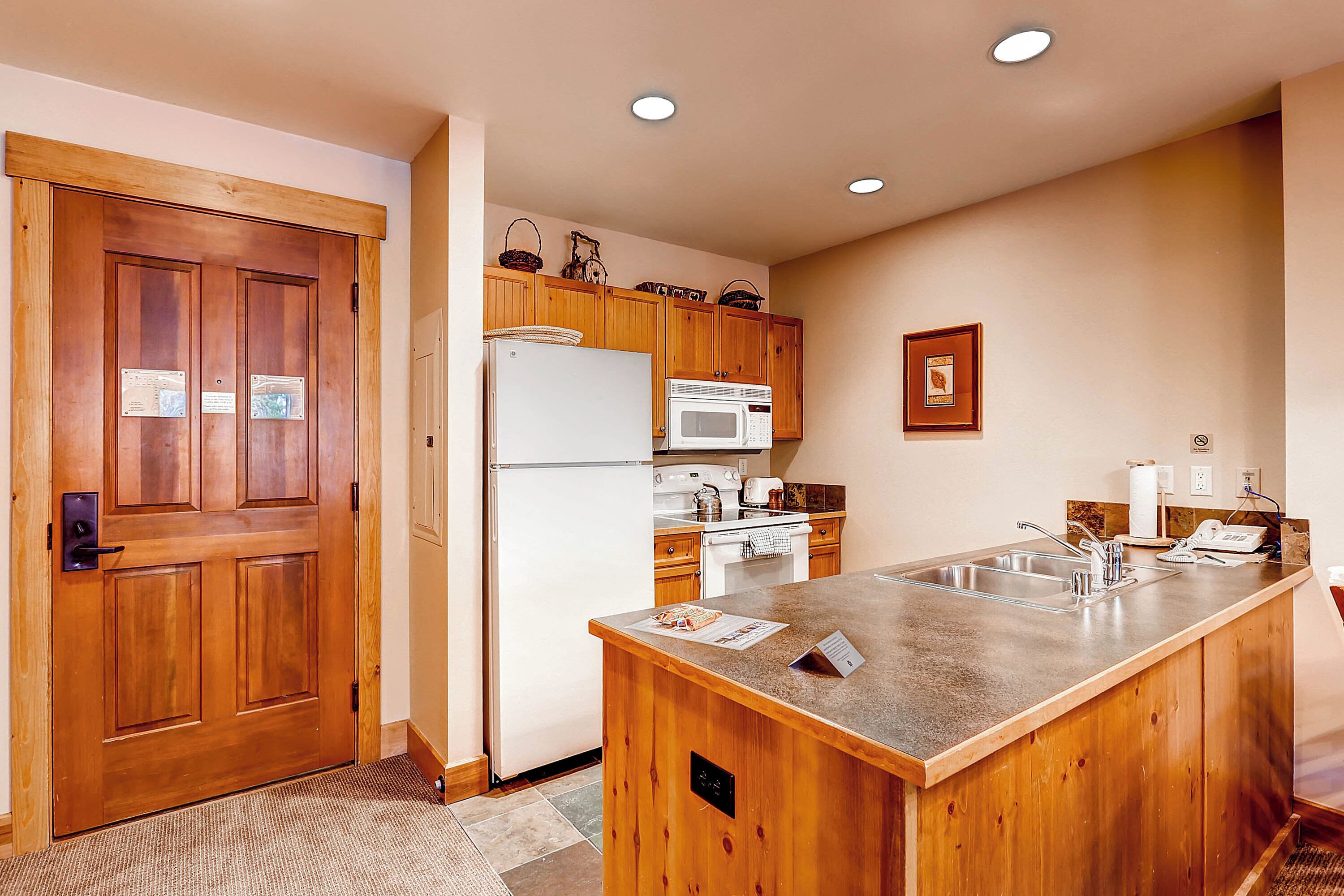 A kitchen with wooden cabinets, a refrigerator, a microwave, and a sink.