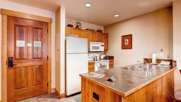A kitchen with wooden cabinets, a refrigerator, a microwave, and a sink.