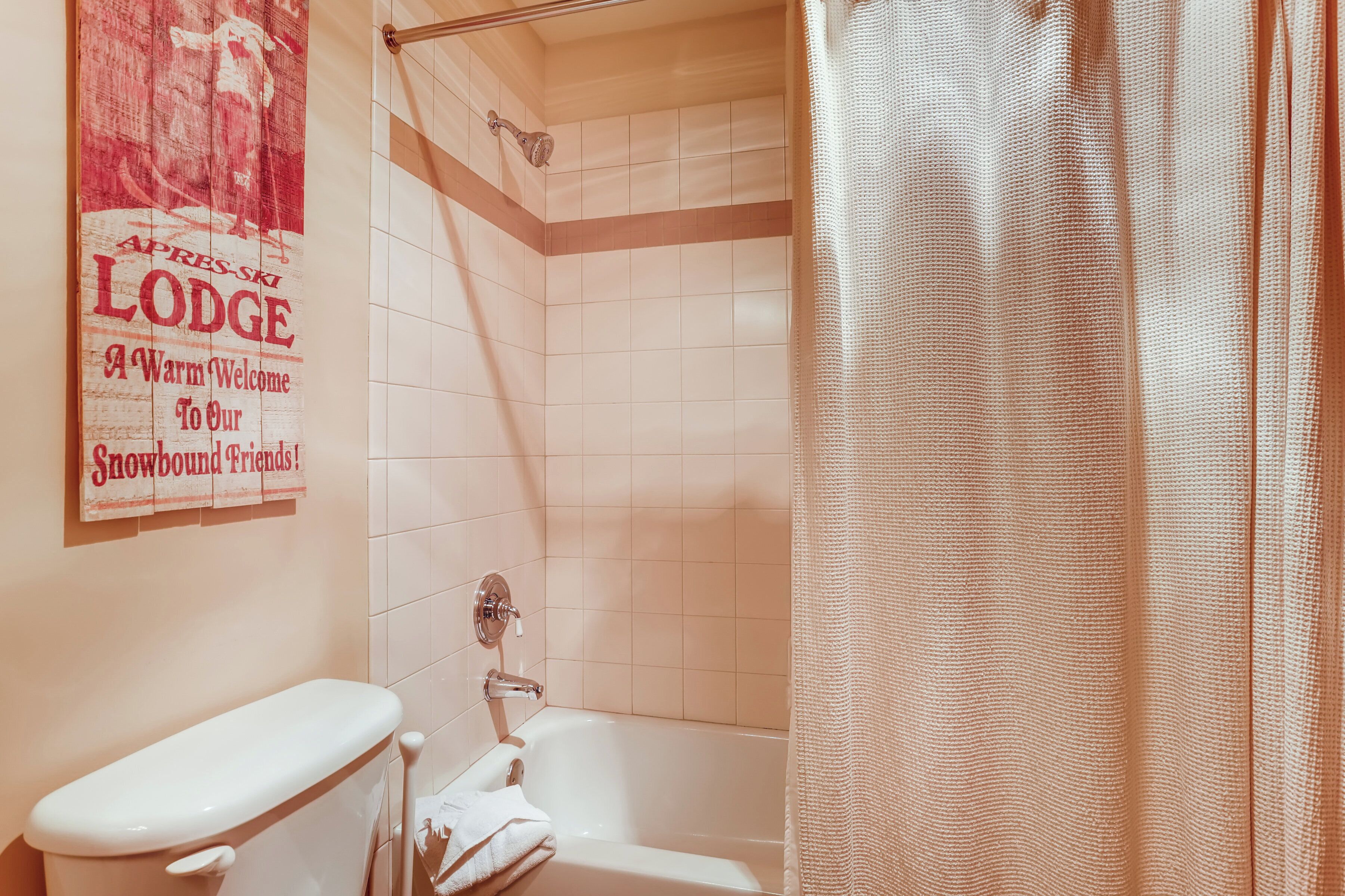Un baño con inodoro, bañera y ducha. Hay un letrero en la pared que dice "APRES-SKI LODGE A Warm Welcome To Our Snowbound Friends!"