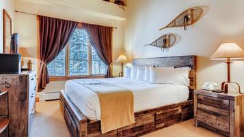 A bedroom with a wooden bed, a desk, a chair, a window with curtains, and a wall-mounted shelf.