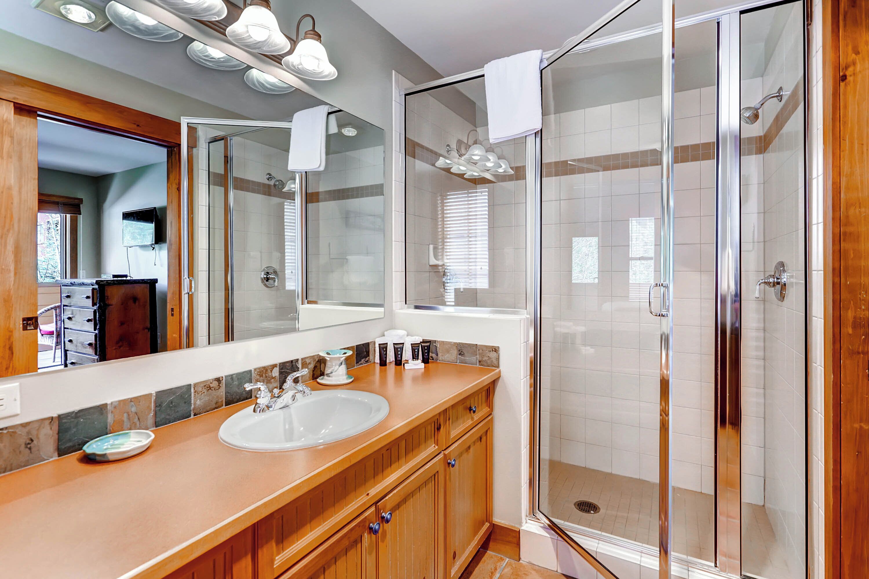 Une salle de bain moderne dotée d’une douche à parois de verre, d’un grand miroir et d’un meuble-lavabo en bois avec un évier et un plan de travail.