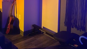 A room with a guitar, a hammock, and a wall with a framed artwork.