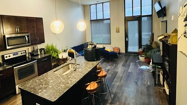A modern kitchen with a central island, dark wood cabinets, stainless steel appliances, and pendant lighting.
