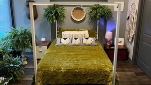 A bed with a green bedspread, two pillows, and two green plants on either side.