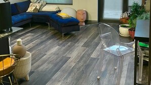 A modern living room with a sectional sofa, a clear glass chair, and a dining area with a table and chairs.