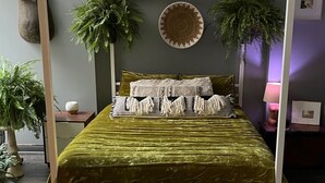 A bed with a green velvet cover, white and black striped pillows, and two large potted plants on either side.