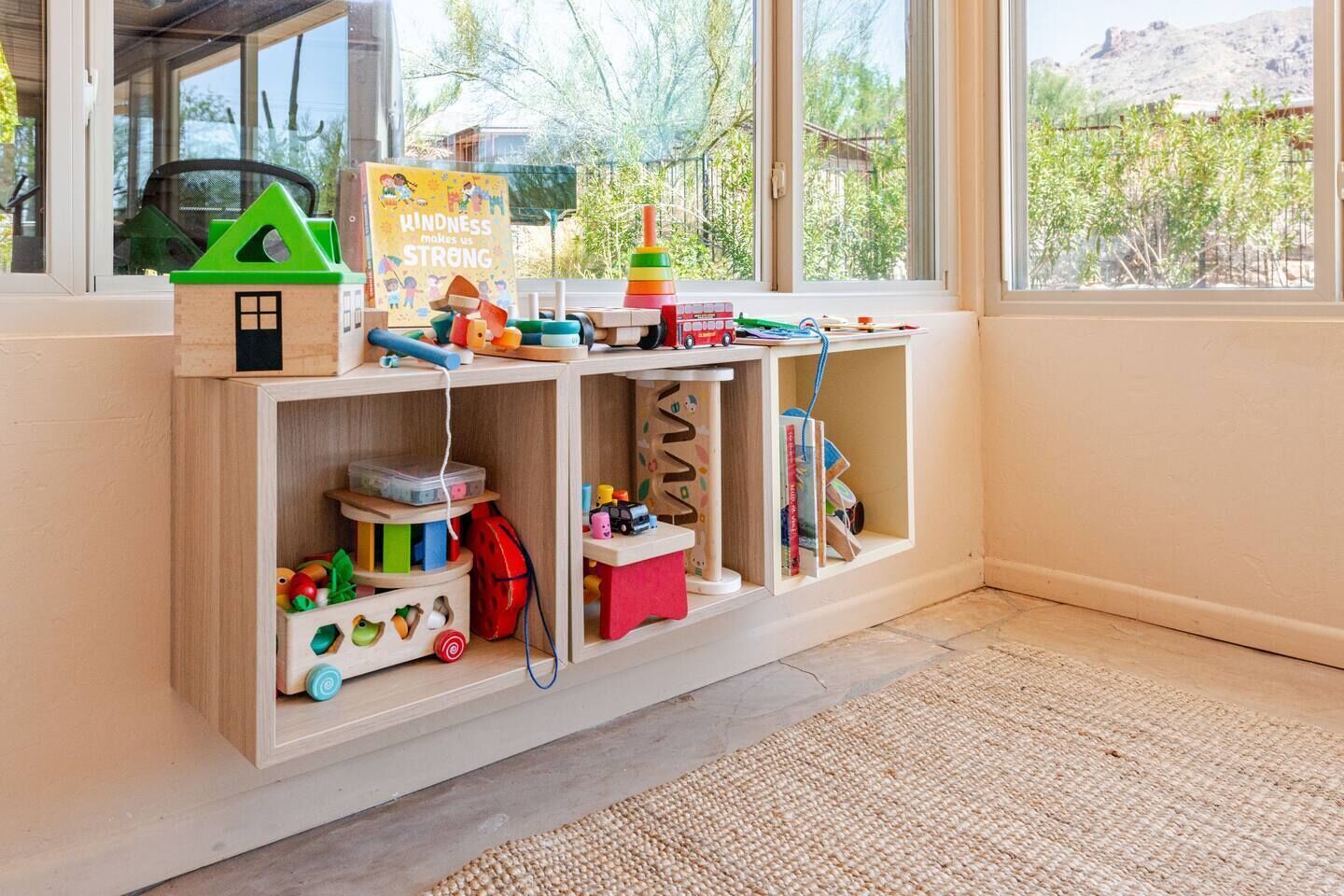 Un espace de jeux pour enfants avec une bibliothèque, des jouets et une vue sur l’extérieur.