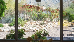 A dining area with a table, chairs, a vase with flowers, and a view of a mountainous landscape through large windows. - Hacienda Riad: free pool heat, hot tub, views (Tucson)