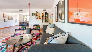 A modern living room with a sofa, chairs, a coffee table, and a colorful rug. There are shelves with decorative items and framed pictures on the walls. - Hacienda Riad: free pool heat, hot tub, views (Tucson)