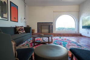 Una sala de estar con un sofá, sillones, una mesa de centro, una alfombra colorida, una chimenea y un televisor montado en la pared.