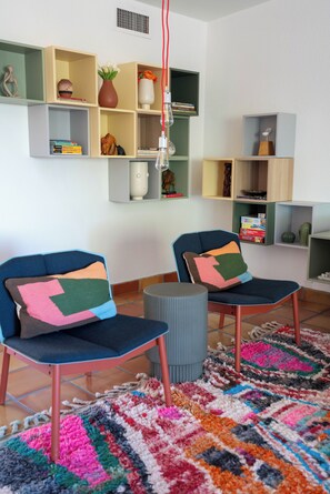 Una sala de estar moderna con dos sillones azules, un tapete colorido y diversos objetos decorativos en estanterías.