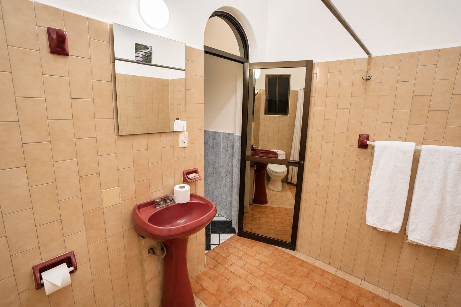 A bathroom with a red sink, a mirror, a toilet, and a shower area.