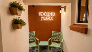Un pequeño espacio al aire libre con dos sillas y un letrero de neón que dice 'MEXICOLINDO Y QUERIDO'.