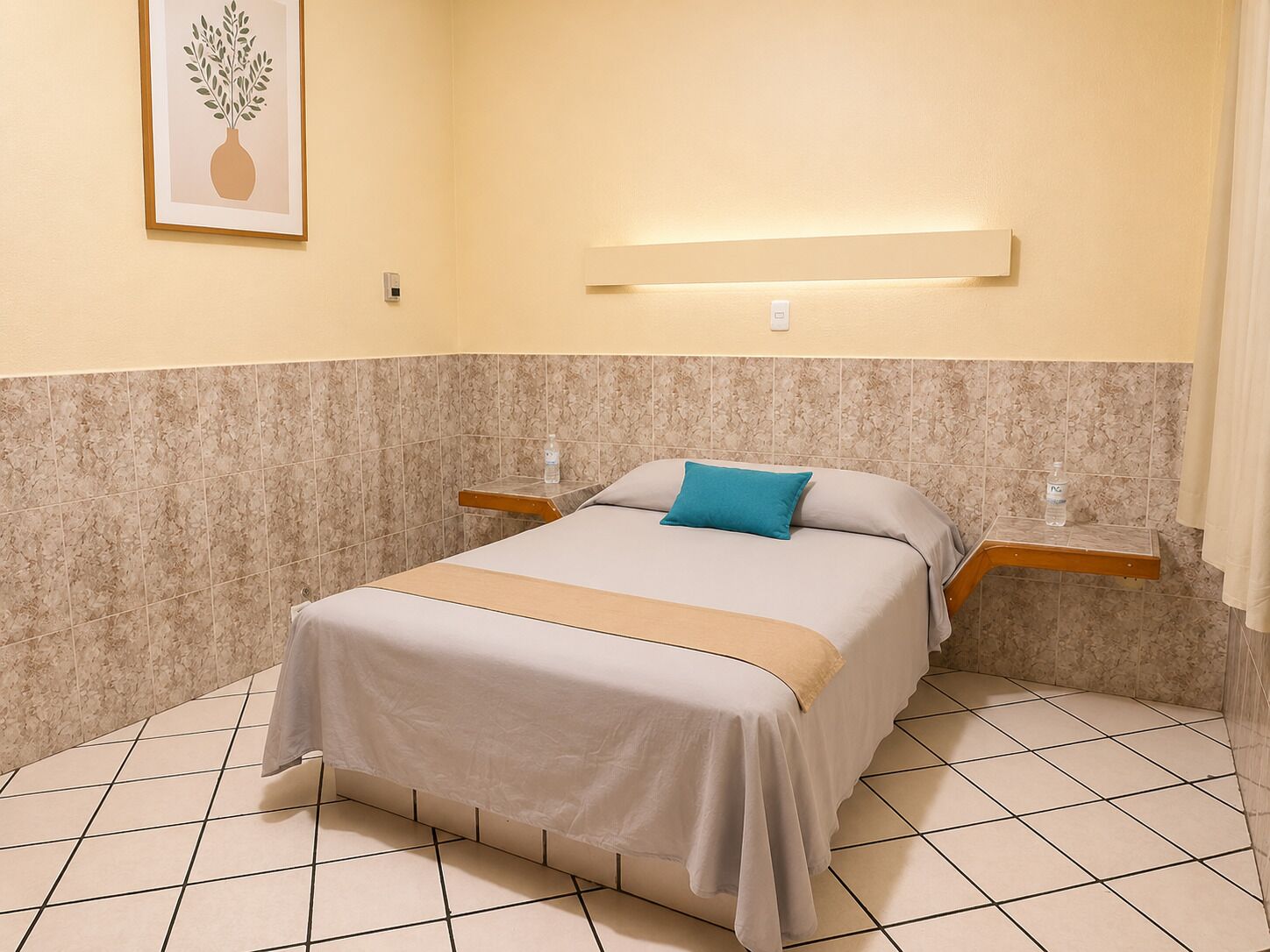 A hotel room with a bed, a bedside table, a wall-mounted light, and a framed picture on the wall.