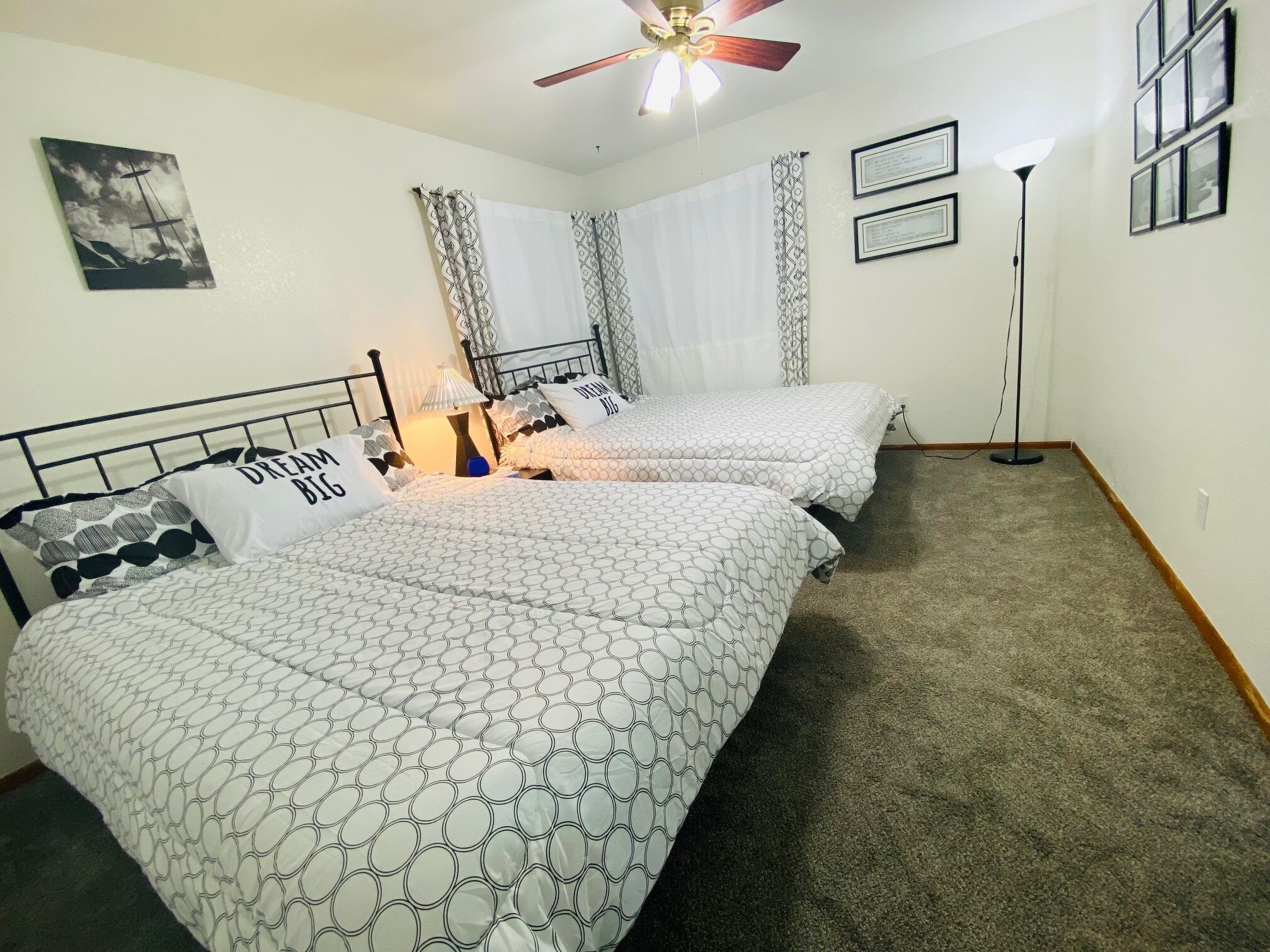 Een slaapkamer met twee bedden, een plafondventilator, een nachtkastje met een lamp en een ingelijst certificaat aan de muur.