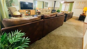 A living room with a brown leather sofa, a television, a fireplace, and a ceiling fan.