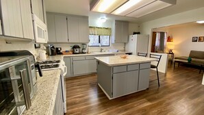 A modern kitchen with grey cabinets, a central island, and a dining area with a sofa and coffee table.