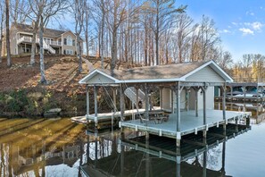 A house with a dock extending into a calm body of water, surrounded by trees and a clear sky. - Waterfront Oasis! Ready to Make a Splash? (Louisa)