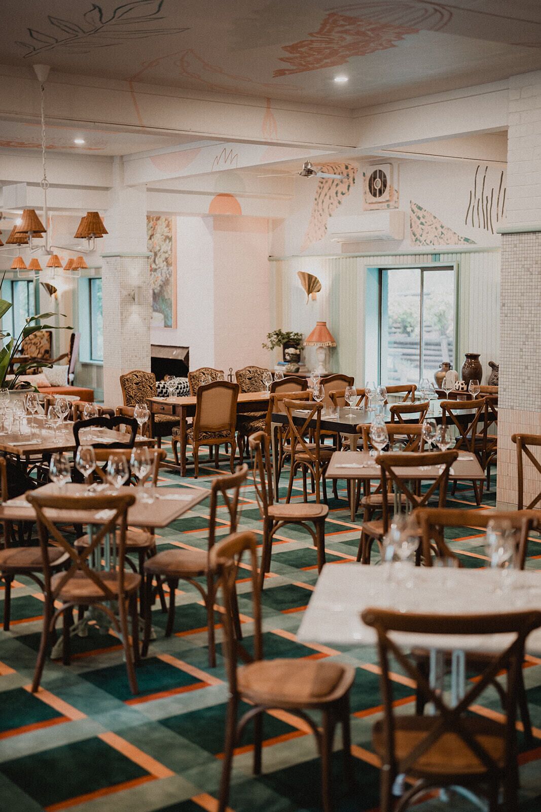 A restaurant with multiple tables and chairs, a patterned carpet, and decorative wall art.