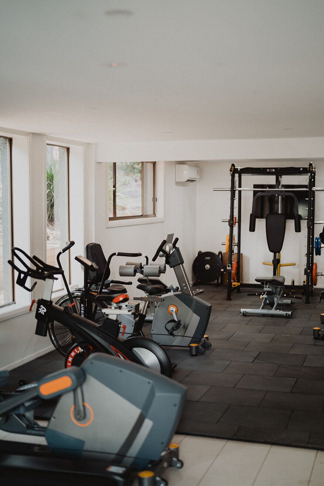Un gimnasio con diversos equipos de ejercicio, incluyendo cintas de correr, una bicicleta estática y una estructura para sentadillas.