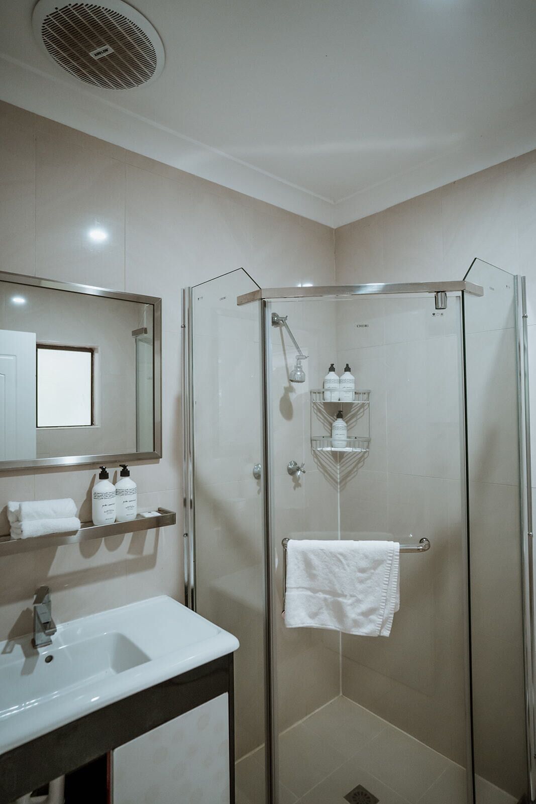 Un baño moderno con ducha envuelta en vidrio, un lavabo blanco y un espejo sobre el lavabo.