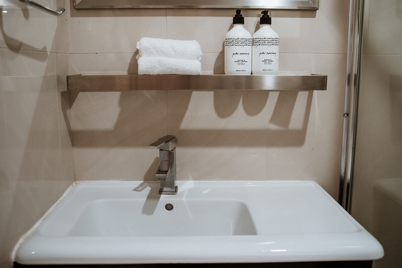 Ein Badezimmer mit einem weißen Waschbecken, einem Handtuchhalter und zwei Flaschen Hand- und Körperseife.