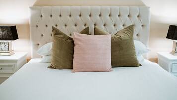 A neatly made bed with a tufted headboard, two bedside tables with lamps, and a clock on one of the tables.