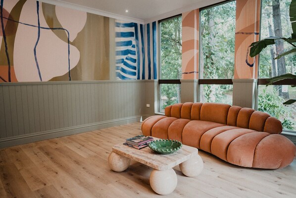A modern living room with a wooden floor, a round orange sofa, and a wooden coffee table with books and a bowl. - The Lodge Jamberoo (Jamberoo)