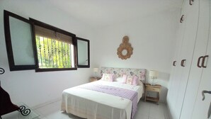 Une chambre à coucher comprenant un lit, deux tables de chevet, une fenêtre avec des stores et une armoire.
