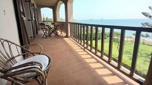 Un balcon avec vue sur la mer, agrémenté de meubles en osier et doté d’un sol carrelé.